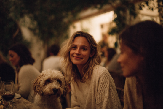 A young woman and a white dog at a dinner table.